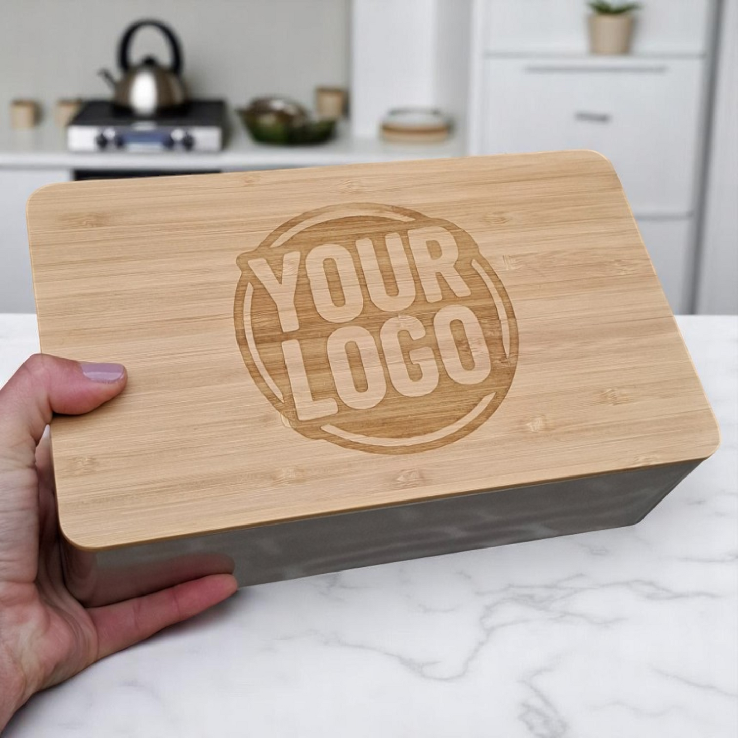 Gravierbare Logokeks-Dose mit Holzdeckel-Frühstücksbrettchen und individuellem Logo, gehalten von einer Hand vor moderner Küchenkulisse – ideal als stilvolles Kundengeschenk