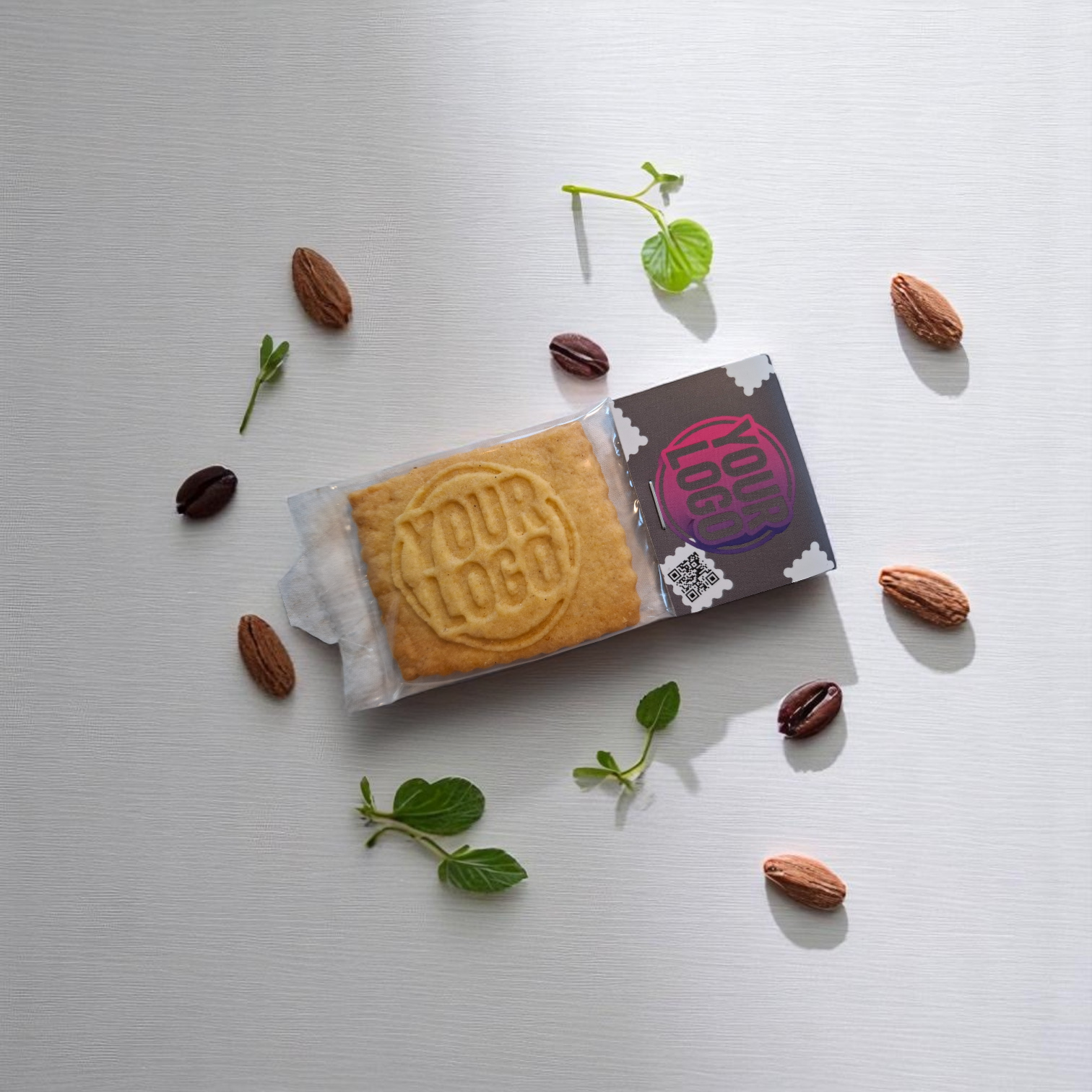 Einzeln verpackter Logokeks mit individuell bedrucktem Keksreiter, dekorativ angerichtet mit Kakaobohnen, Mandeln und Minze – ideal als Streuartikel oder Messegeschenk mit QR-Code