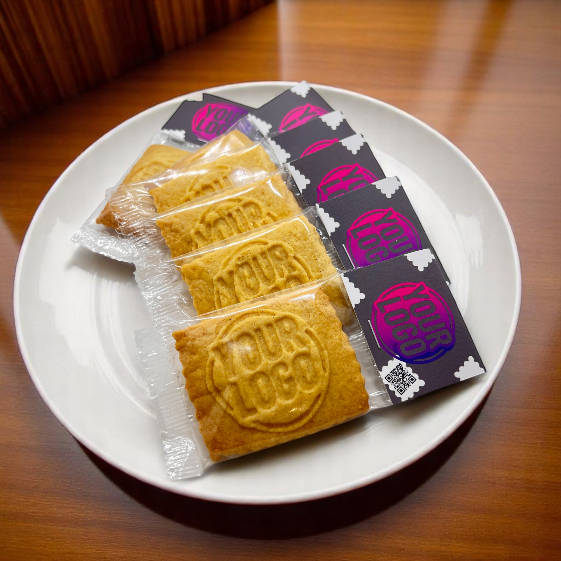 Fünf einzeln verpackte Logokekse mit individuell bedrucktem Label, angerichtet auf einem Teller – optimal als Giveaway oder Branding-Element im Hotel- und Gastrobereich