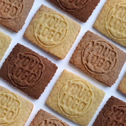 Unverpackte Logokekse in verschiedenen Sorten wie Schokolade, Vanille, Karamell und Spekulatius diagonal auf weißem Untergrund – nachhaltige Wahl für Gastronomie und Events
